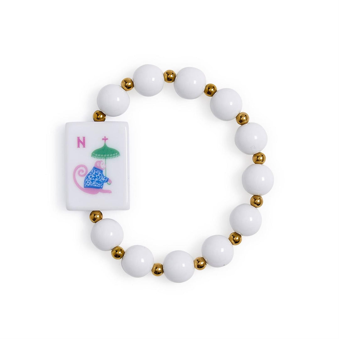 Mahjong Beaded Stretch Bracelet with alternating white and gold beads, a rectangular tile featuring a blue and pink monkey holding a green umbrella next to the red letter “N,” and vibrant acrylic accents. Available in multiple sizes.