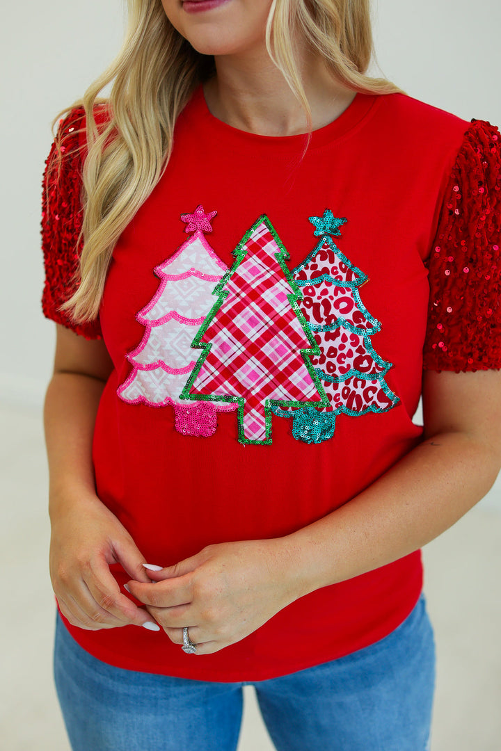 Relaxed-fit red sequin short-sleeve top featuring three decorative Christmas tree appliqués in plaid, leopard, and chevron patterns.