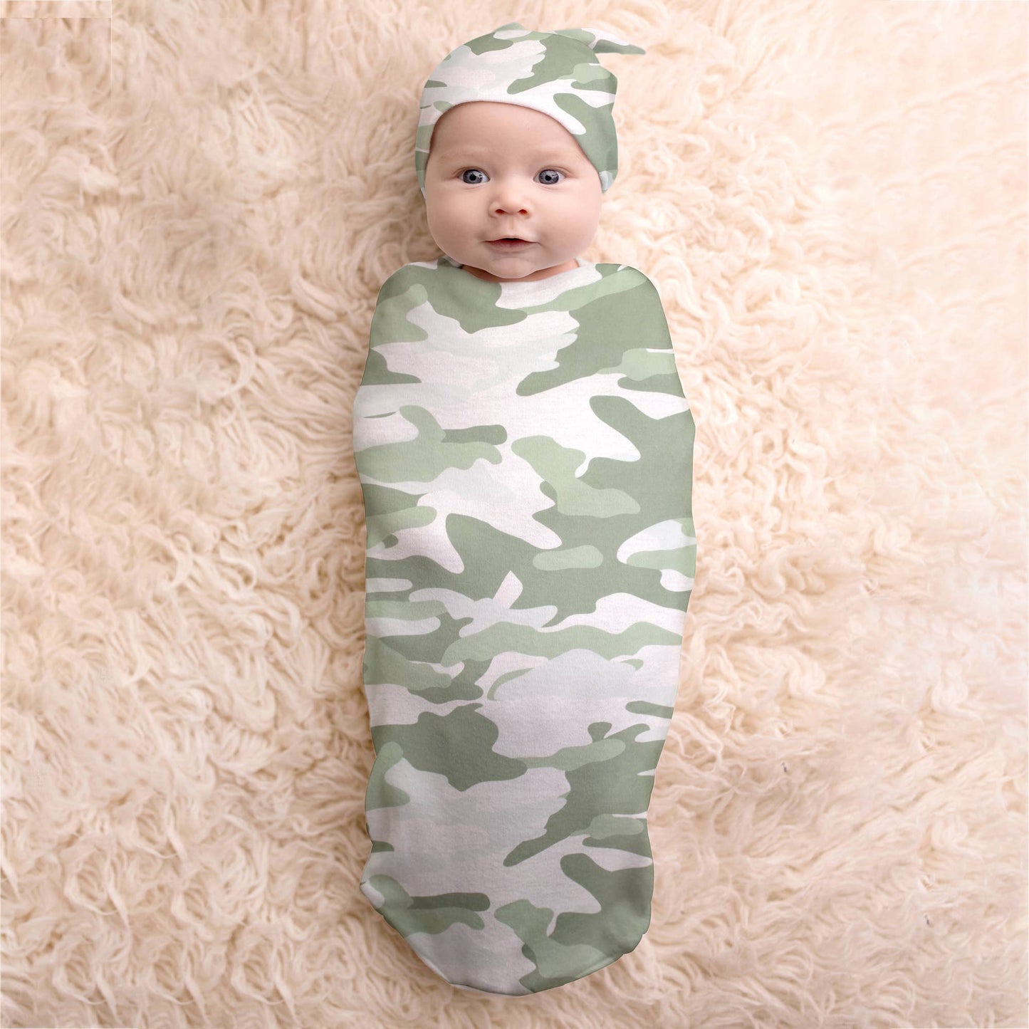 Baby in camo cocoon with matching hat on a white faux fur rug.