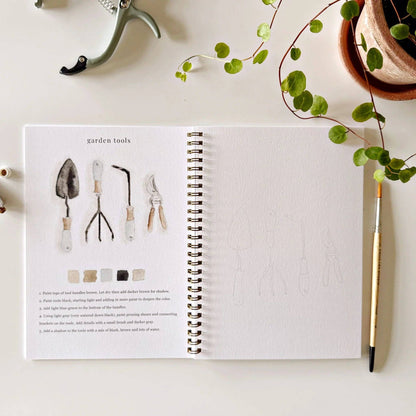 The Garden Watercolor Workbook open to garden tool illustrations and outlines for practice. Available in 8x10 and 9x12 inches.