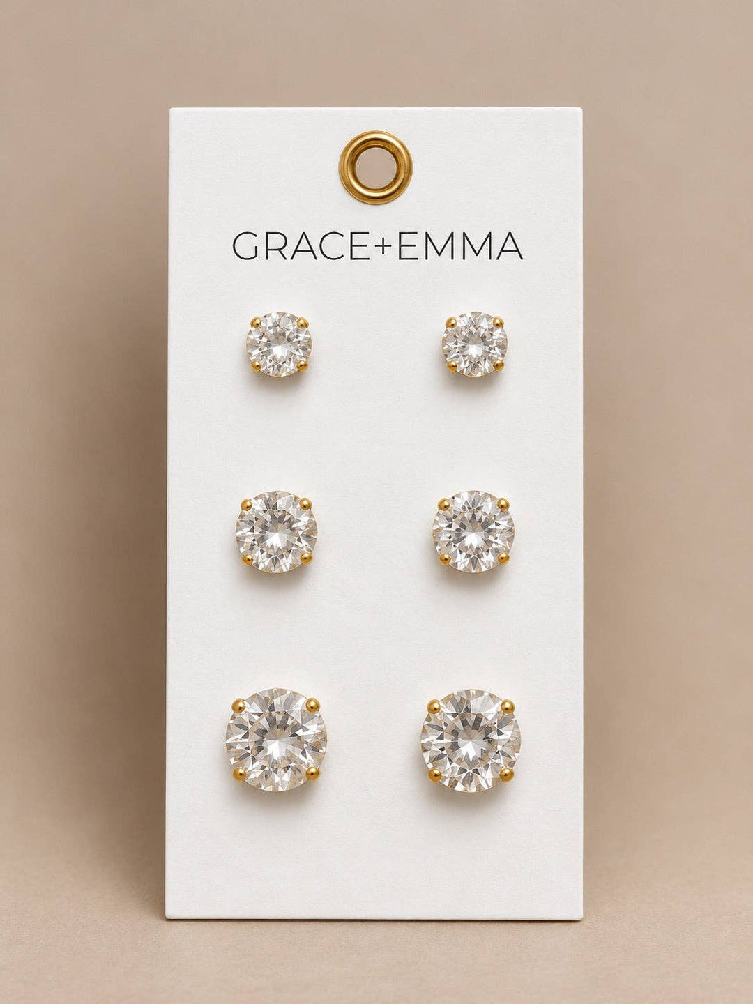 Three pairs of round, clear stone earrings in gold-tone settings.