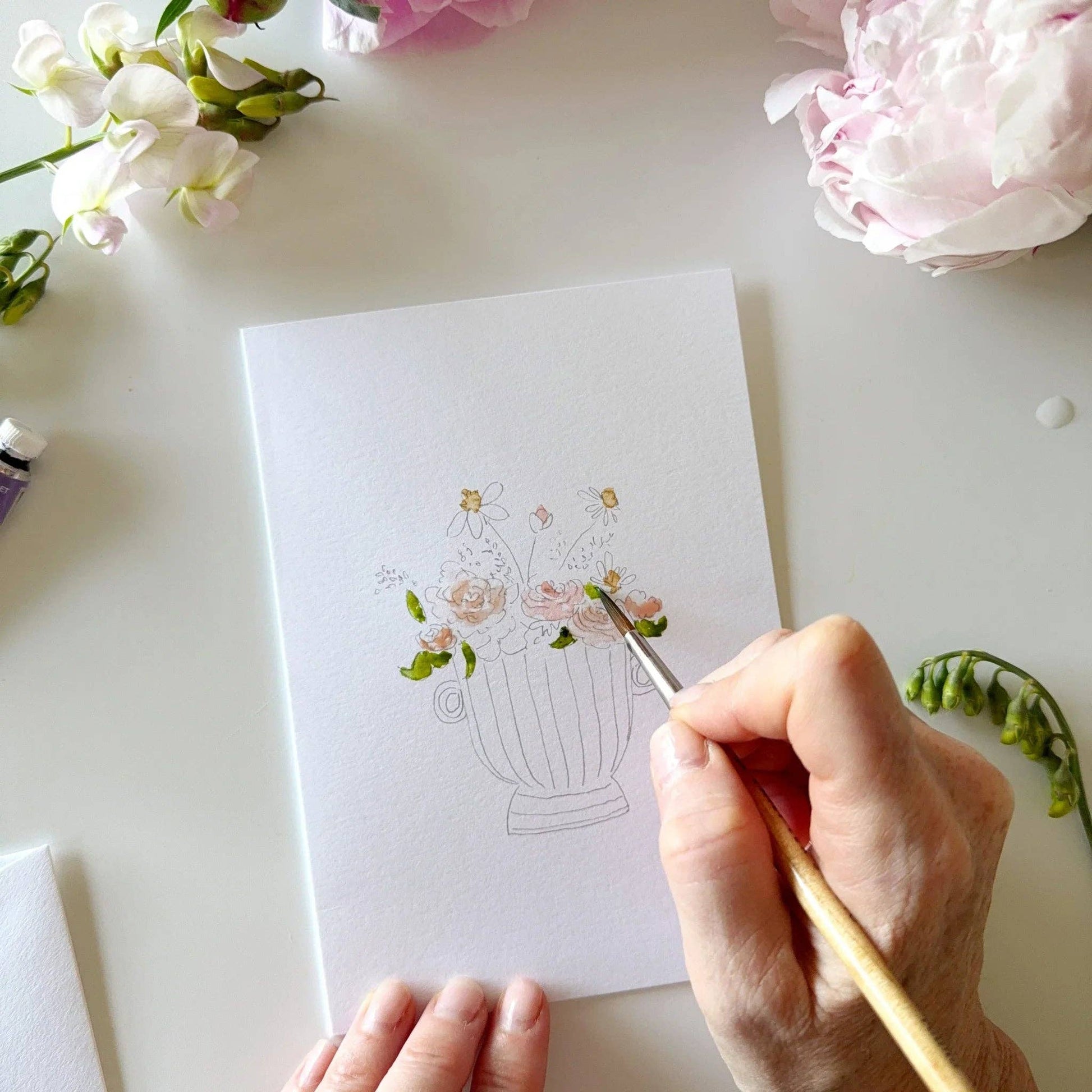 A hand paints floral designs on a Bouquets paintable watercolor notecard. Set includes DIY greeting cards available in multiple sizes.