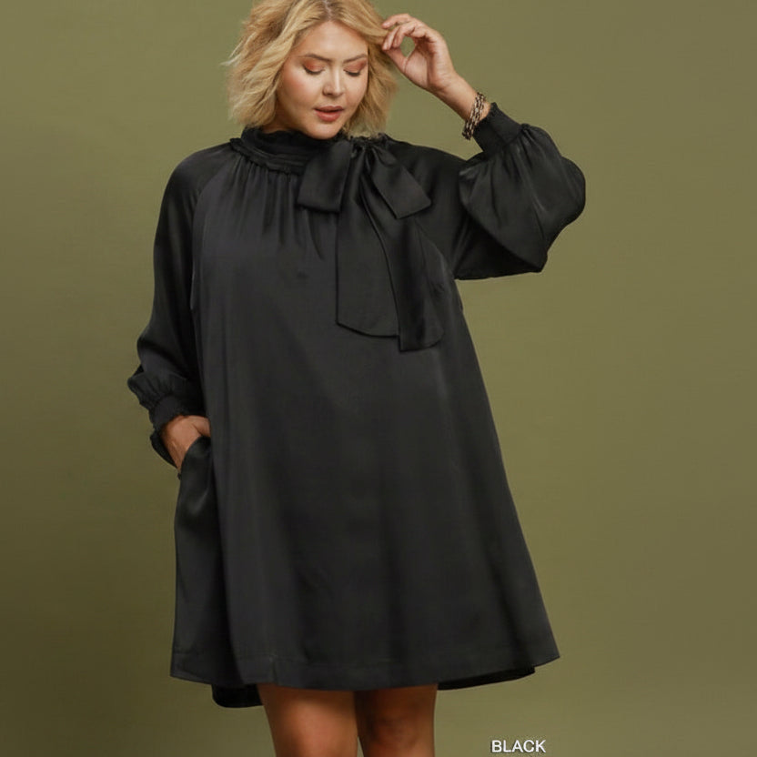 Satin Tie Neck Dress: a loose-fitting black satin mini dress with long sleeves, dramatic tie neck bow, and side pockets. Available in plus sizes.
