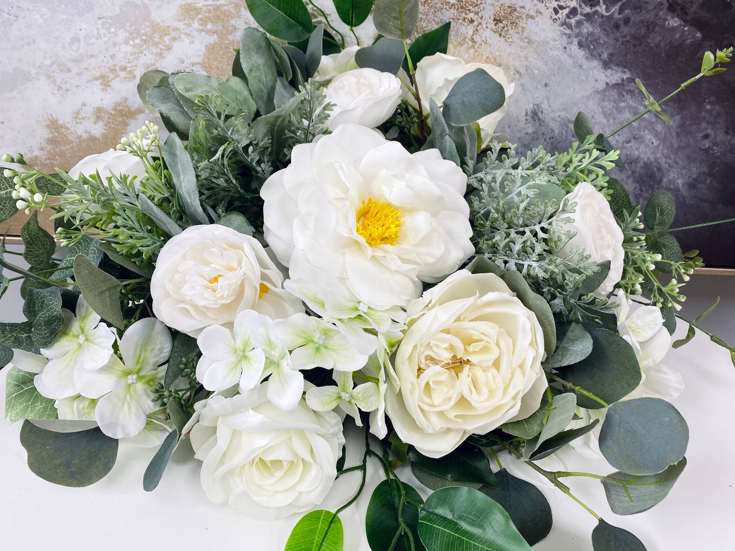 A vibrant floral arrangement with lifelike Real Touch Orlane Rose (15" long) in pure white, peonies, and greenery including eucalyptus and broad leaves. Features lush blossoms with yellow stamens.