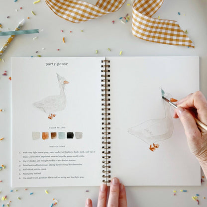 An open Celebrate watercolor workbook featuring a goose illustration, color palette, and beginner-friendly painting instructions. Available in multiple sizes.