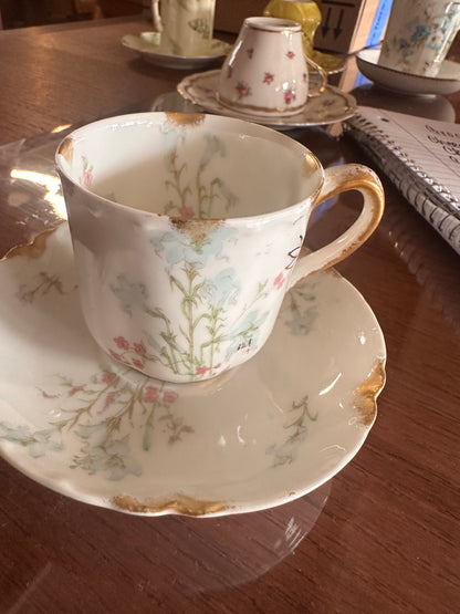 Antique hand-painted porcelain demitasse cup and saucer with floral designs and gold accents. Size: demitasse.