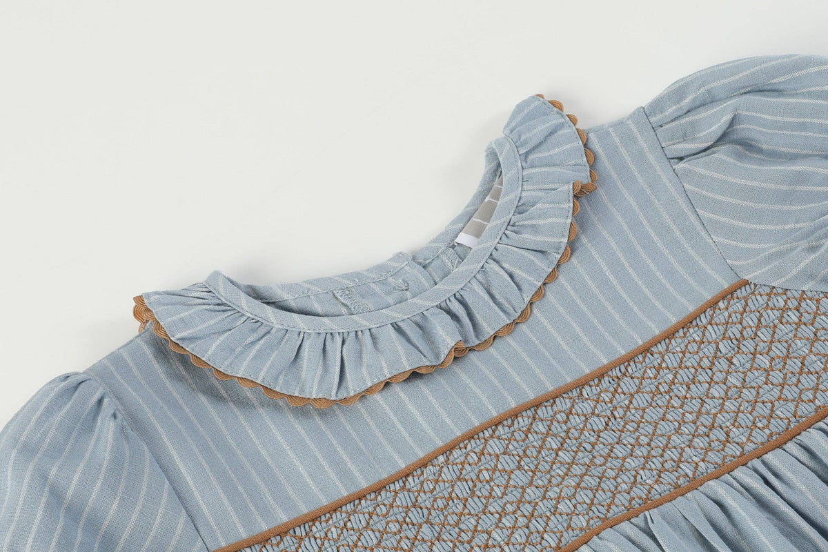 Light blue dress with white pinstripes, brown-trimmed smocked ruffle collar, puffed sleeves, and brown geometric smocking on the chest. Available in size 18-24M.