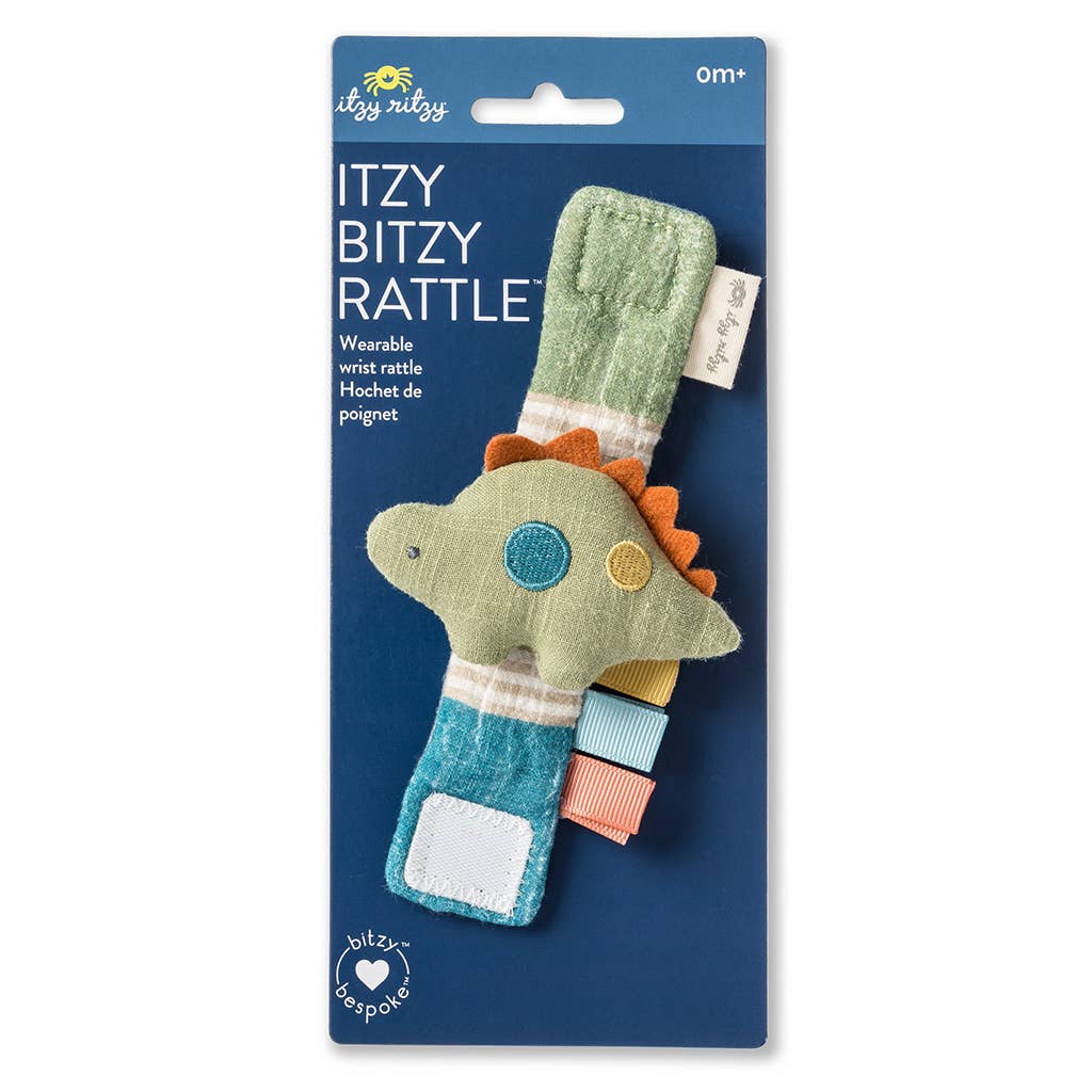 A Itzy Bitzy Cottage wrist rattle made from natural cotton fabric, packaged on a blue cardboard hanger, shaped like a colorful elephant with green, orange, and blue details, labeled for ages 0 months