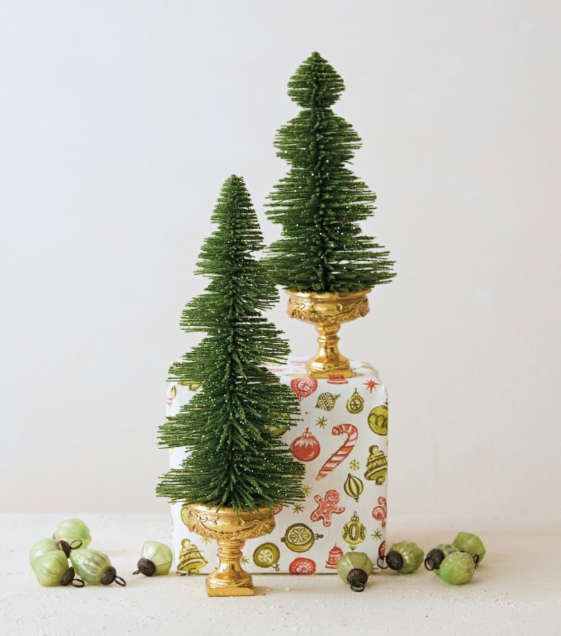 Two green glittered bottle brush trees on gold pedestal stands.