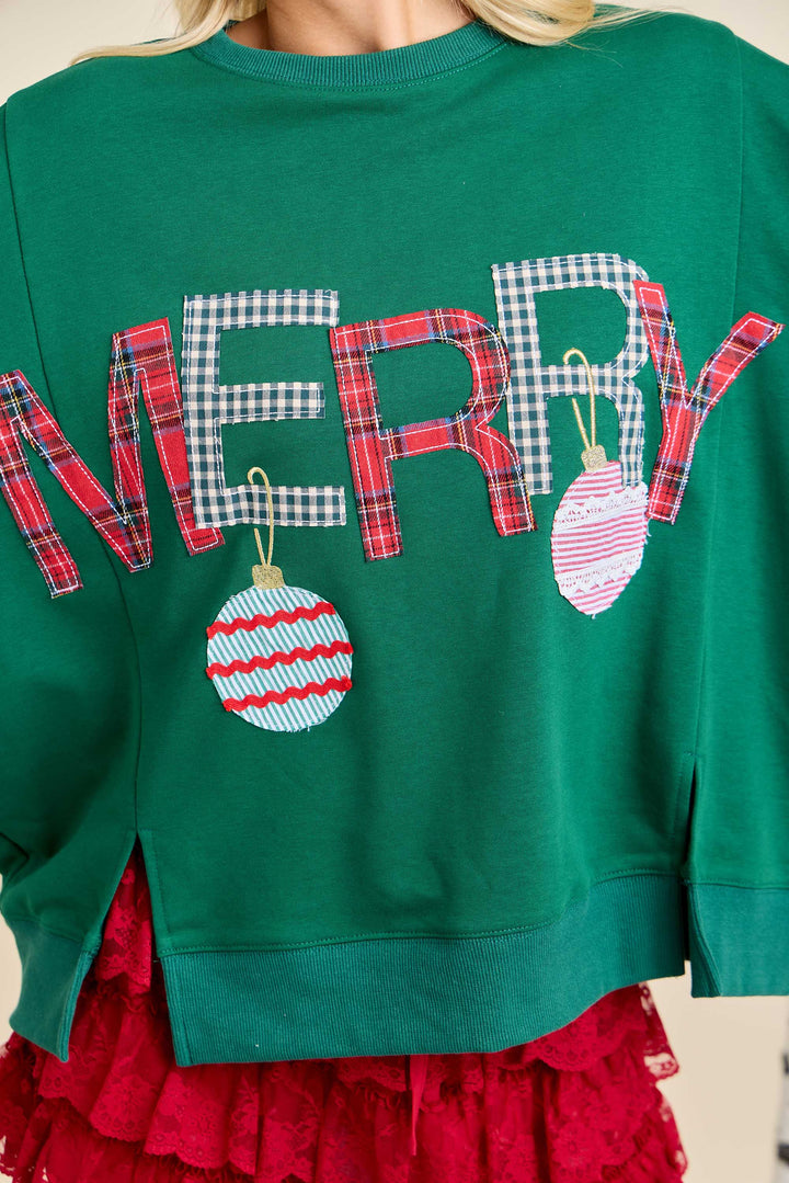 “Merry With Ornament Patchwork Oversized Long Sleeve Top” in hunter green, features plaid “MERRY” lettering and two ornament applique designs. Available in sizes S-XXL.