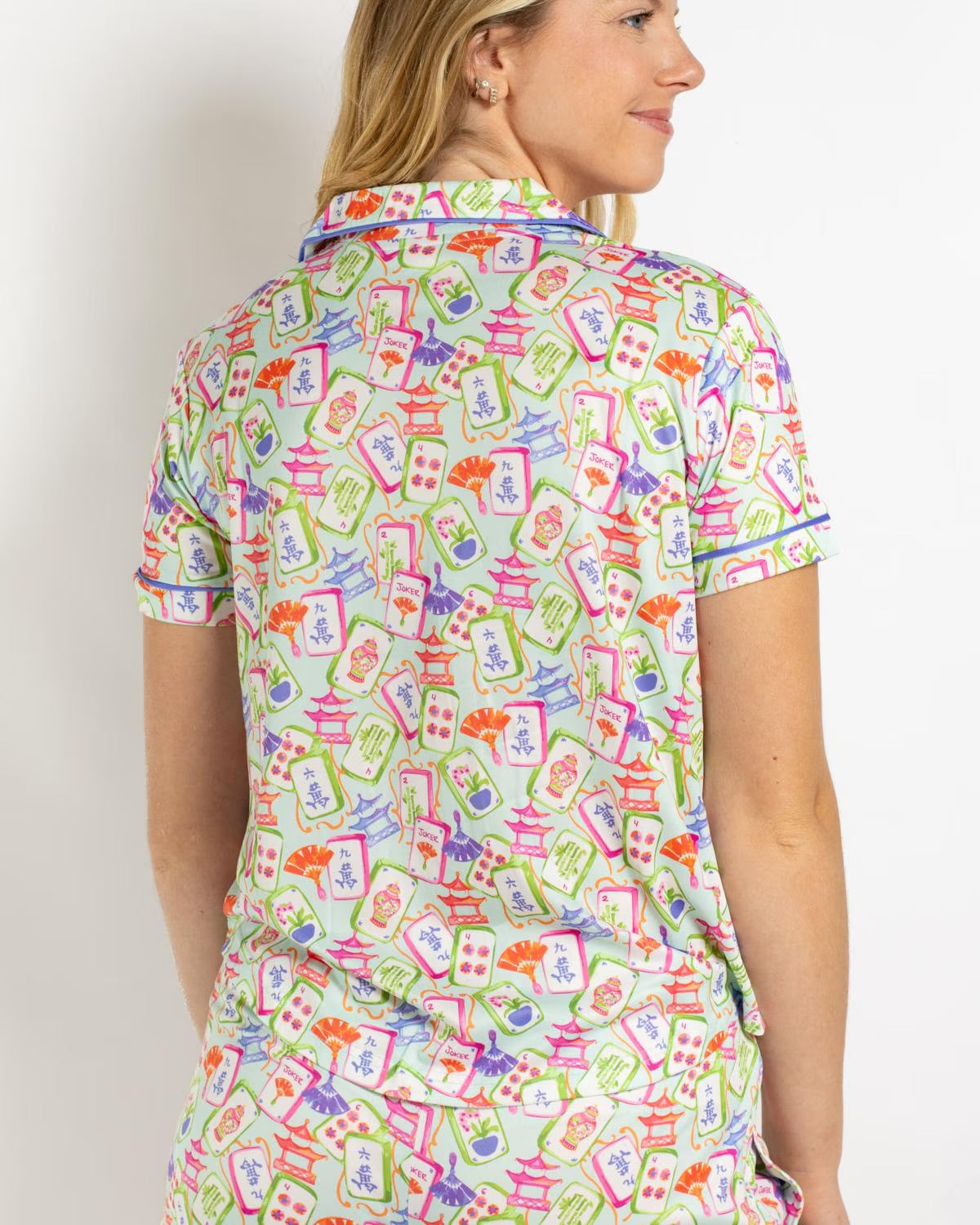 Mahjong Dreams Short Sleeve Shirt with a lively pattern of pagodas, fans, and abstract designs in pink, green, blue, orange, and red on a white background. Available in sizes XS-XL.