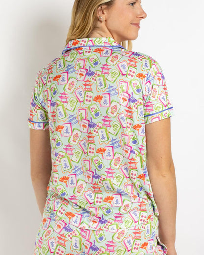 Mahjong Dreams Short Sleeve Shirt with a lively pattern of pagodas, fans, and abstract designs in pink, green, blue, orange, and red on a white background. Available in sizes XS-XL.