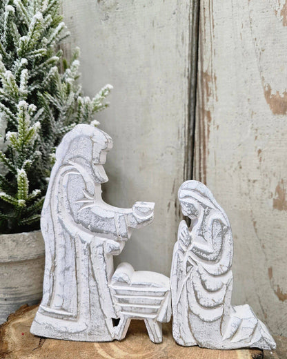 The Nativity Trio 6.5x8in includes white wooden figurines of Mary kneeling, Joseph standing, and baby Jesus in a manger.