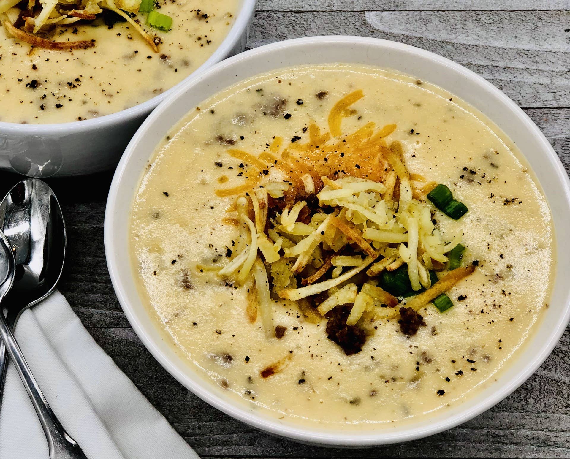 Classic Cheeseburger Soup Mix in two bowls, topped with cheese, meat, and green onions. Available in 16oz and 32oz sizes.