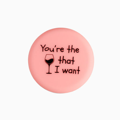 Pink circular wine bottle stopper with "You're the [wine glass] that I want" text. Sizes available: standard bottle fit.