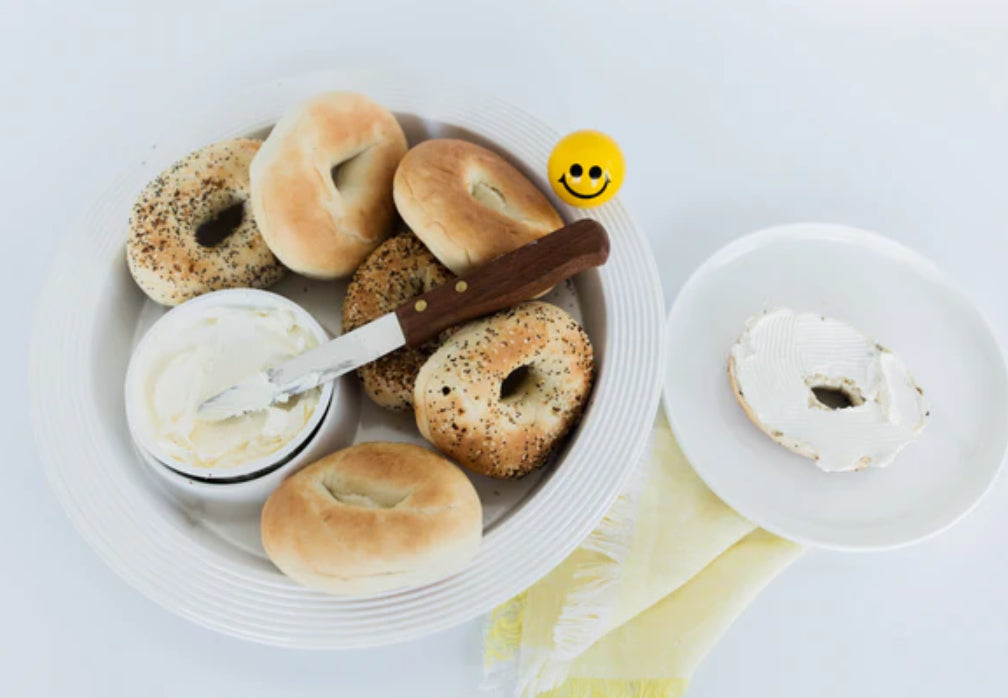 **Chip and Dip Platter Pinstripes**
- A white plate featuring several bagels, a small bowl of cream cheese, and a knife.
- Includes one bagel with cream cheese spread on one half.
- Sizes available: One size.