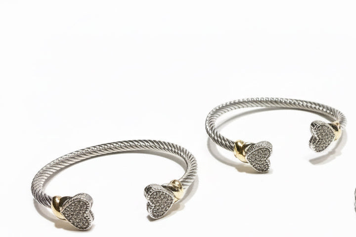 Two twisted silver heart bangles with gold accents and sparkling stone tips; available in small, medium, and large sizes.
