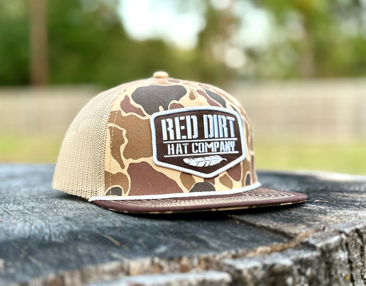 The Old Skool Camo hat by Red Dirt Hat Company features brown/tan camo, mesh back, logo patch. Available in S/M, L/XL.