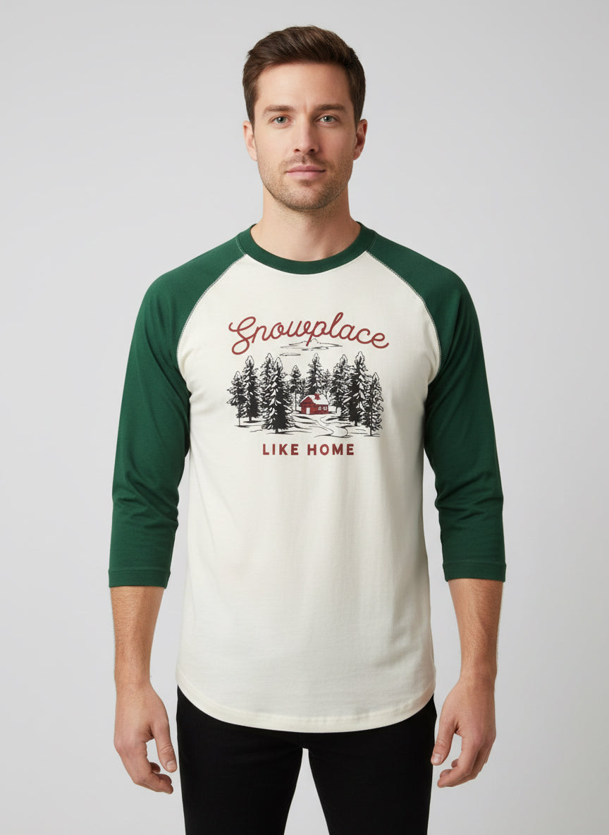 Men’s Snow Place Like Home Baseball T-Shirt in cream with green three-quarter sleeves, featuring a snowy cabin graphic and “Snowplace LIKE HOME” text.