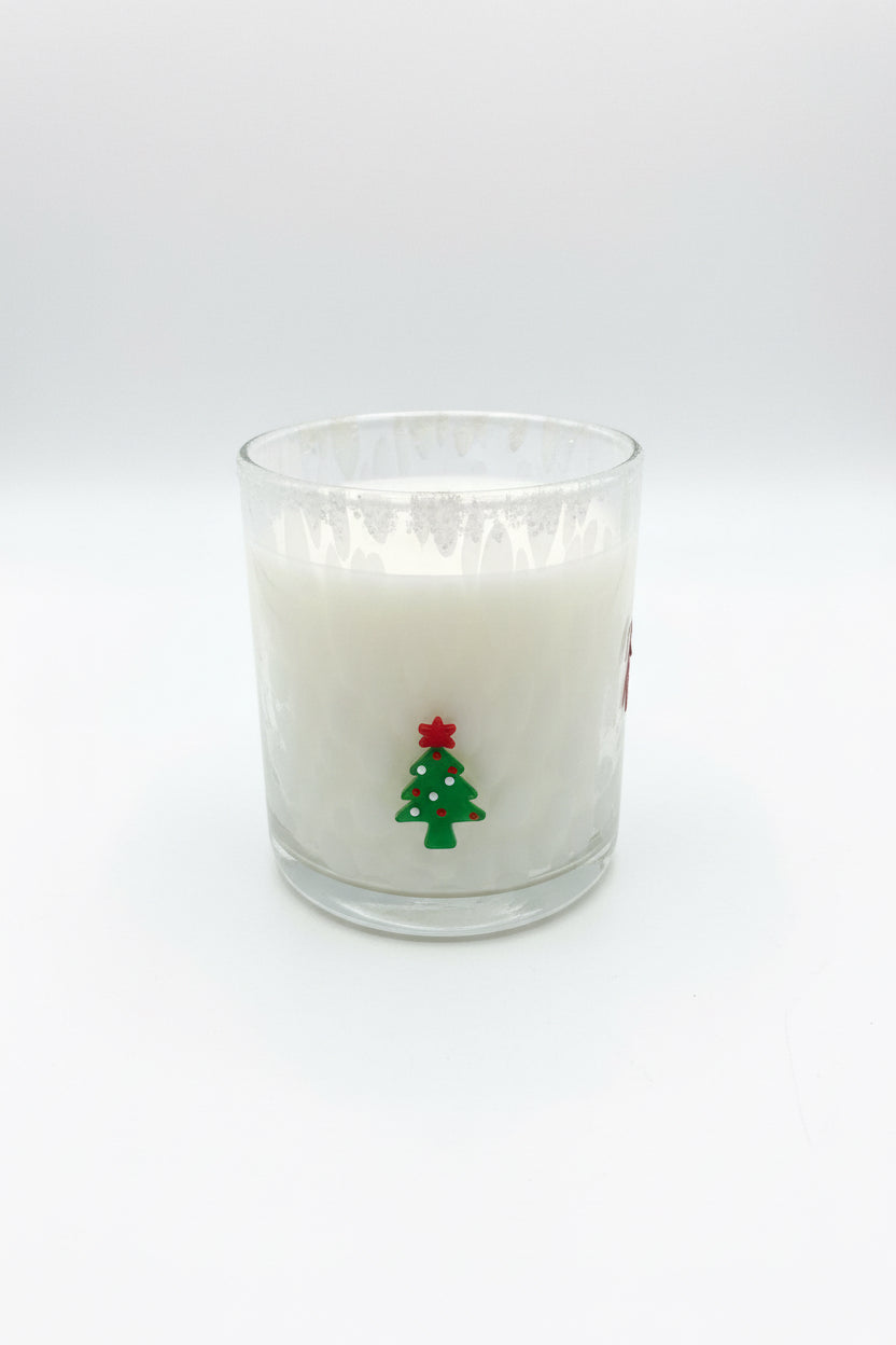 The Holiday Soy Candle features white soy wax in a glass holder decorated with a small green Christmas tree and a red star. Available in multiple sizes.