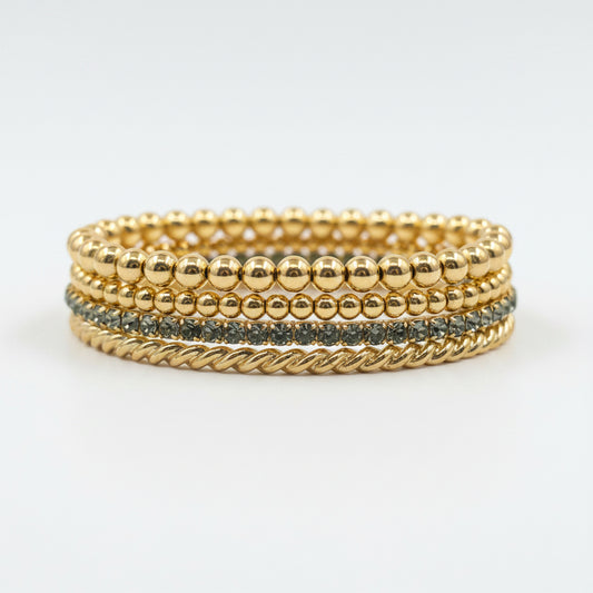 Logan Multi Strand Bracelet Stack: four gold bracelets—three with beads, one twisted rope, and one with small blue inlaid stones. Available sizes: S, M, L.