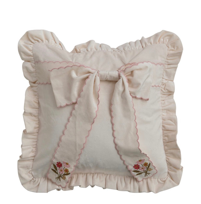 Light cream throw pillow with floral embroidery, central scalloped bow, ruffled edges, and pink scalloped trim. Available in standard and large sizes.