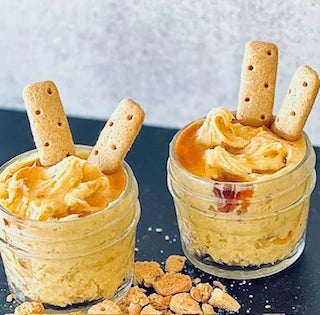 Two small glass jars of Carmie’s Pumpkin Spice Cheesecake Dip topped with caramel sauce and two biscuit sticks each. Available in small size only.