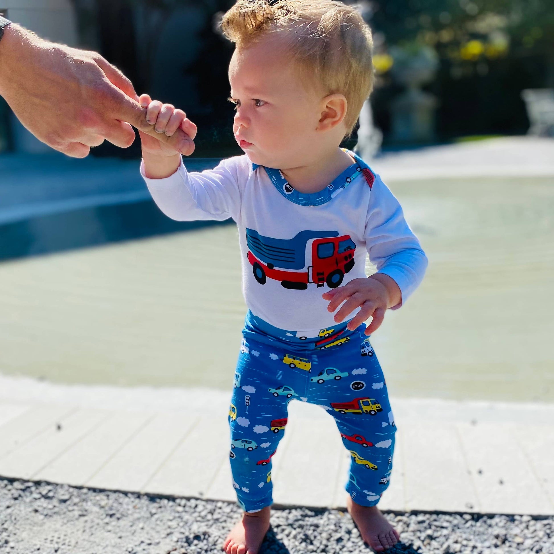 Little boy modeling the onesie and pants outside. Holding hands of guardian to stand up.