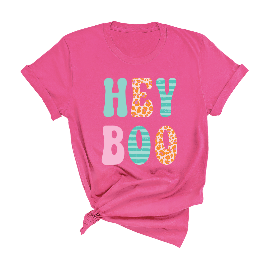 Vibrant pink 100% cotton Bella + Canvas tee with “HEY BOO” in multicolored animal print and stripe letters; features a knotted bottom hem. Available in sizes S–XXL. Designed and printed in the USA.