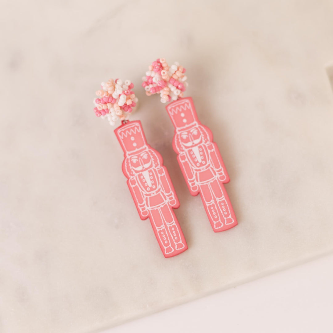 Pink Nutcracker Pom Pom Earrings with nutcracker shapes and beaded floral tops; available in one size.