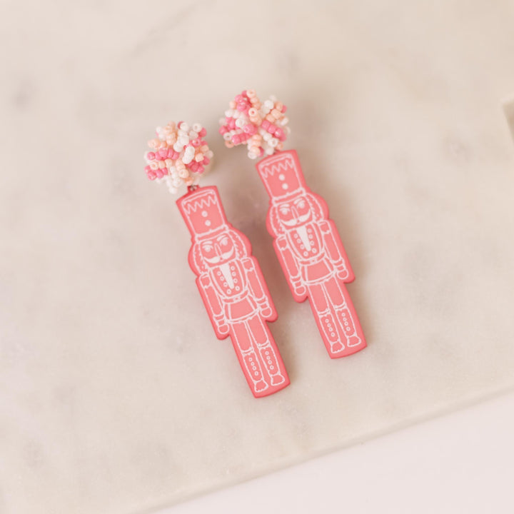Pink Nutcracker Pom Pom Earrings with nutcracker shapes and beaded floral tops; available in one size.