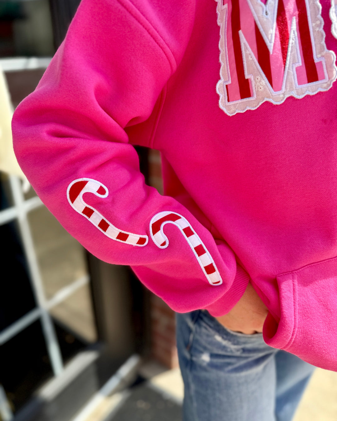 Striped Scallop Merry Hoodie with candy cane sleeve designs and a large “M” on the chest; available in sizes S-XXL.