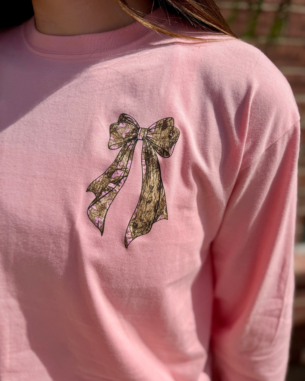 Tree Camo Bow Long Sleeve with black lace bow design on the chest; available in sizes S-XL.