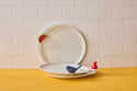 Two white stoneware Celebration Circle Plates with red and blue bird accents on rims. Available in 8" and 10" sizes.