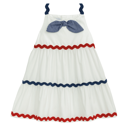 Sleeveless white dress with navy straps, blue gingham bow, red/navy ric rac trim. Sizes: 2T-6X.
