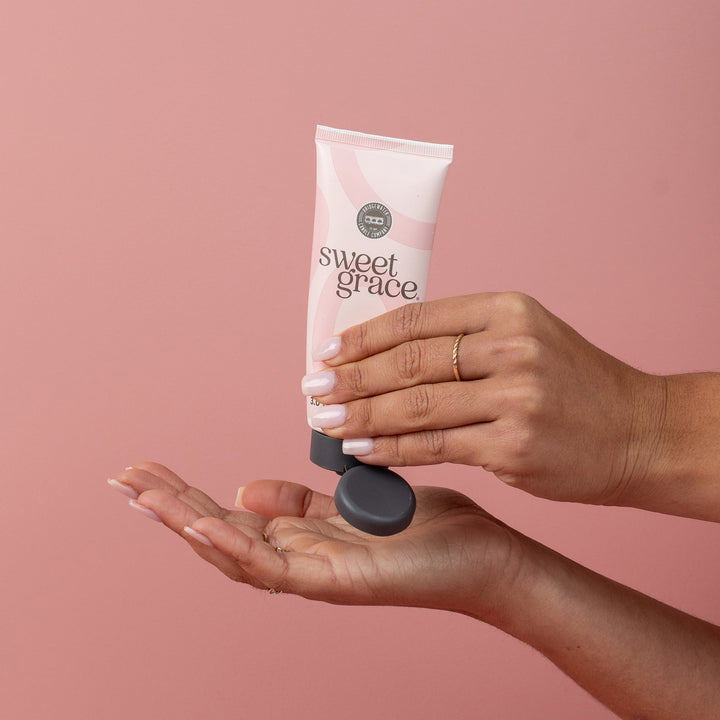 Sweet Grace Hand Cream being dispensed from a pink tube; available in 1.65 oz and 3 oz sizes.