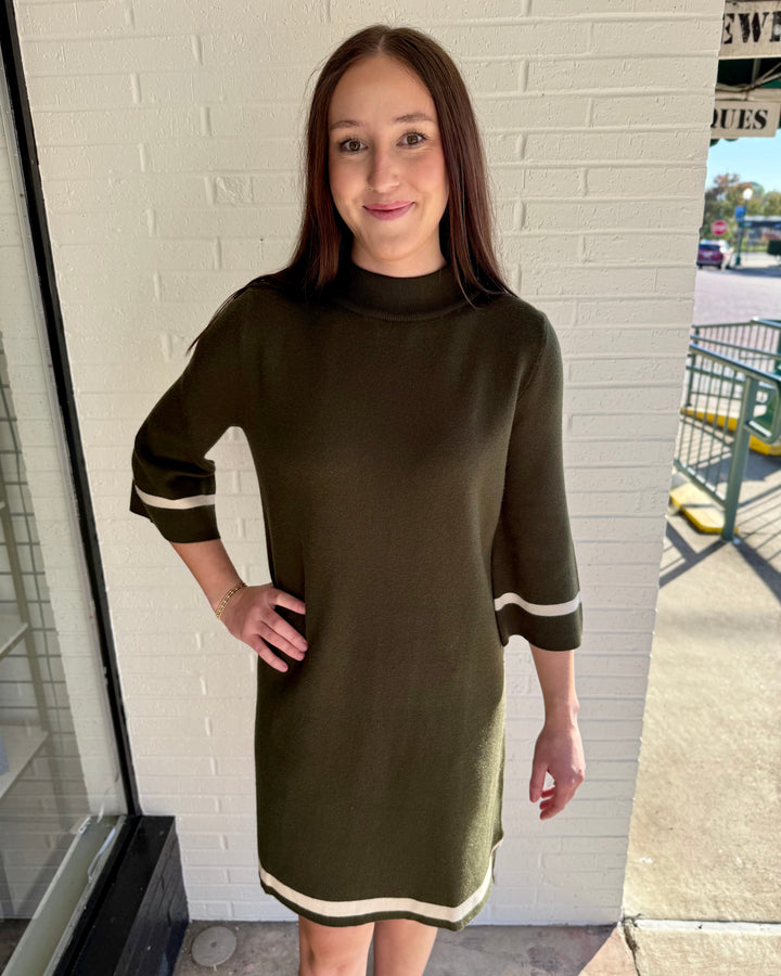 Olive green mock neck sweater dress with three-quarter sleeves and cream contrast trim at cuffs and hem. Available in sizes XS-XL.