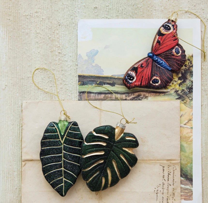 Hand-painted mercury glass butterfly, Alocasia leaf, and monstera leaf holiday ornaments with gold hanging strings.