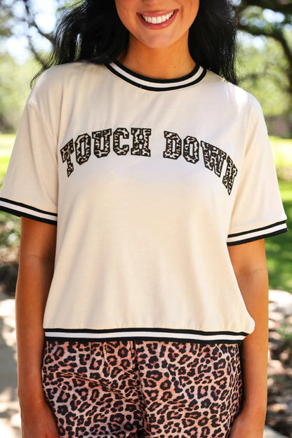 Touch Down Leopard Tee: cream shirt with black trim and bold “TOUCH DOWN” lettering; available in sizes S–XL.