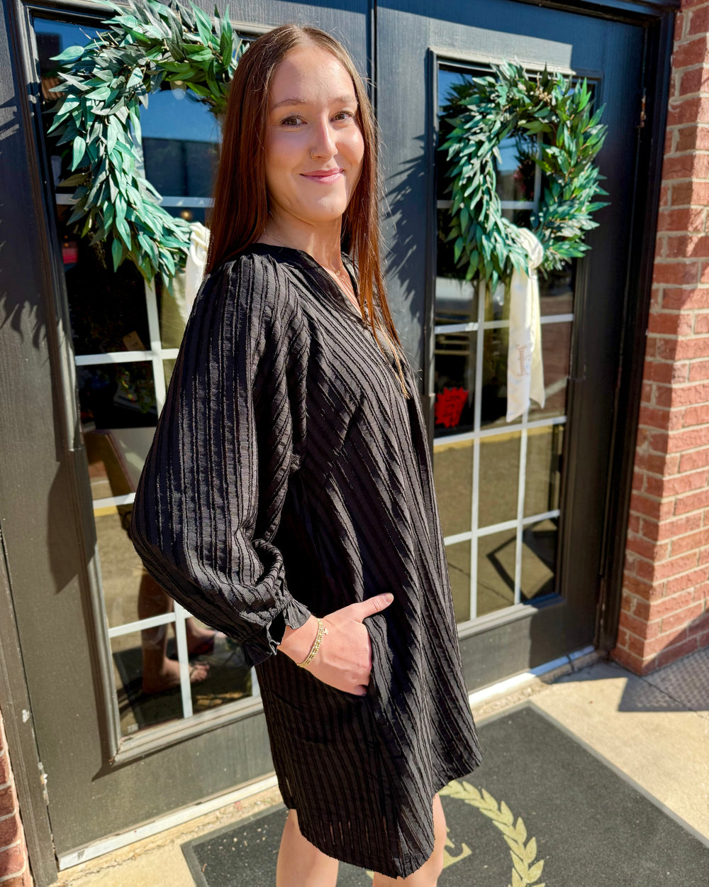 Black cotton V-neck shift dress with long sleeves, textured vertical stripes, and side pockets. Available in all sizes.