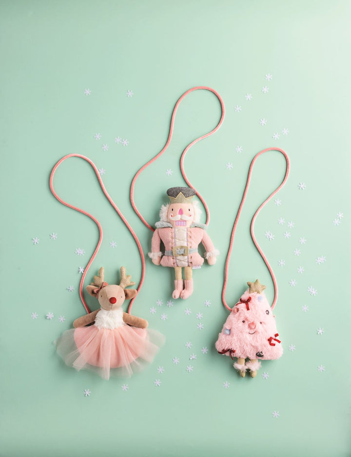 Three plush Christmas purses: reindeer in a tutu, nutcracker, and decorated tree, each with a pink shoulder strap.