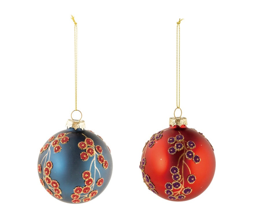 Two round botanical glass ornaments with gold hanging strings: one matte blue with red floral detailing, one red with purple floral detailing.