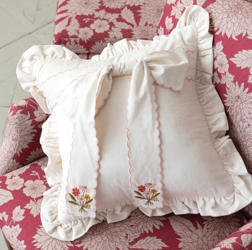 The Scalloped Embroidered Bow Pillow features a large scalloped bow and pink embroidered flowers on white fabric. Available sizes: standard, queen, and king.