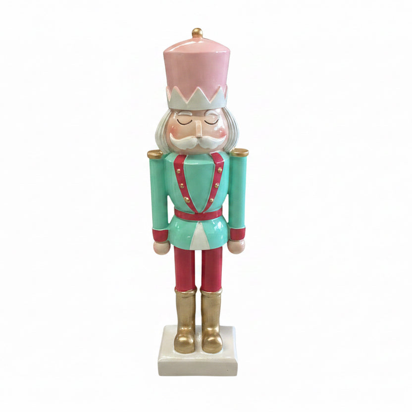 Pink hat, teal jacket, red trousers nutcracker figurine on square base.
