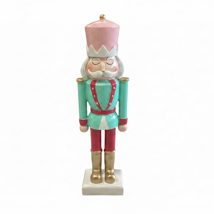 Pink hat, teal jacket, red trousers nutcracker figurine on square base.