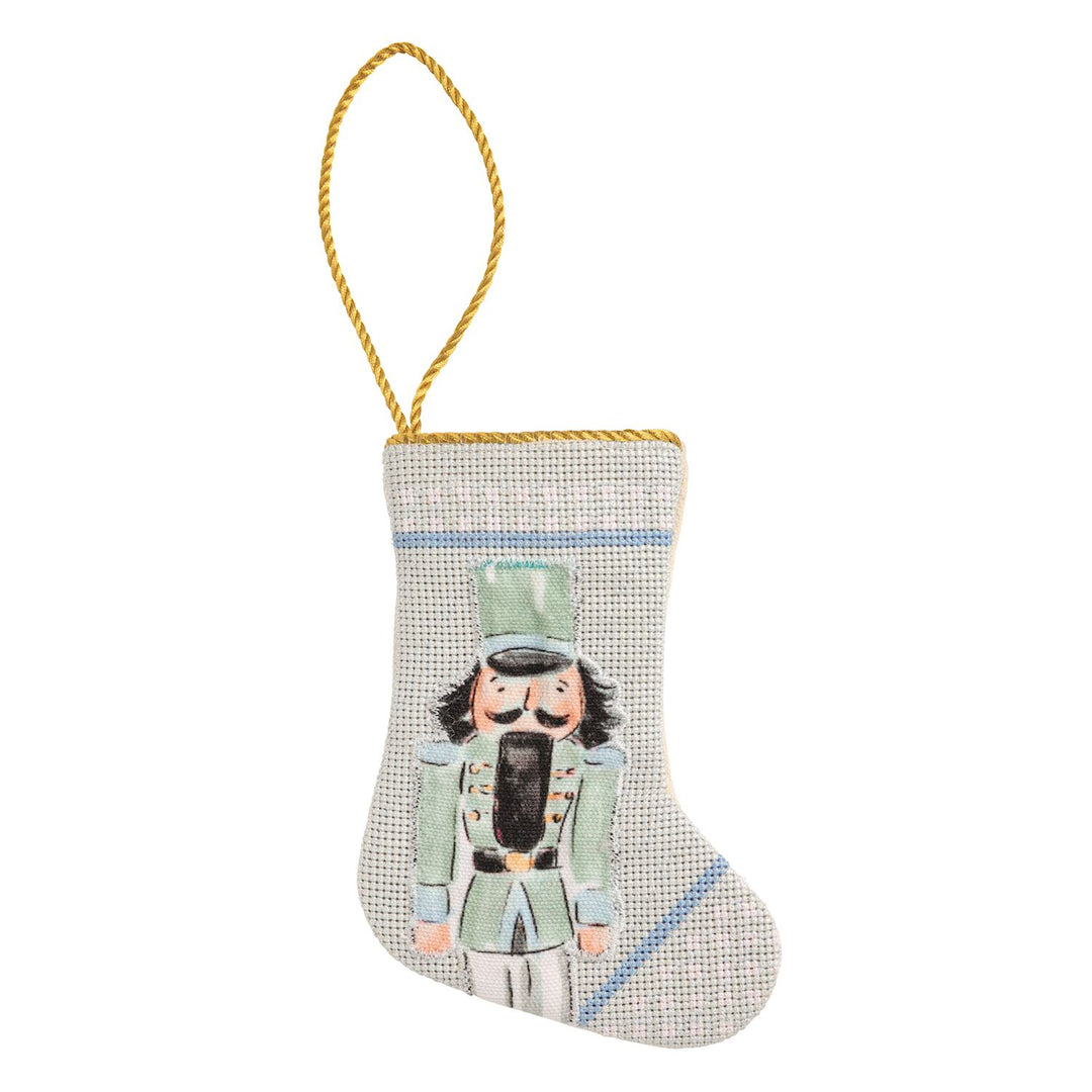 Needlepoint Nutcracker Mini Stocking ornament in a green uniform with a gold hanging cord.