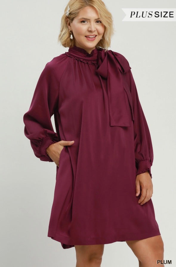 Plus size Satin Tie Neck Dress in rich plum with long sleeves, ruffled collar, and bow tie detail at the neck. Available in sizes 1X–4X.