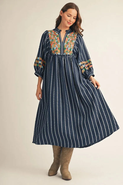 Floral Embroidered Midi Dress: navy blue, long-sleeve, ankle-length midi with white vertical stripes, vibrant floral embroidery on the upper part, and a subtle ruffled neckline. Available in sizes XS-XL.