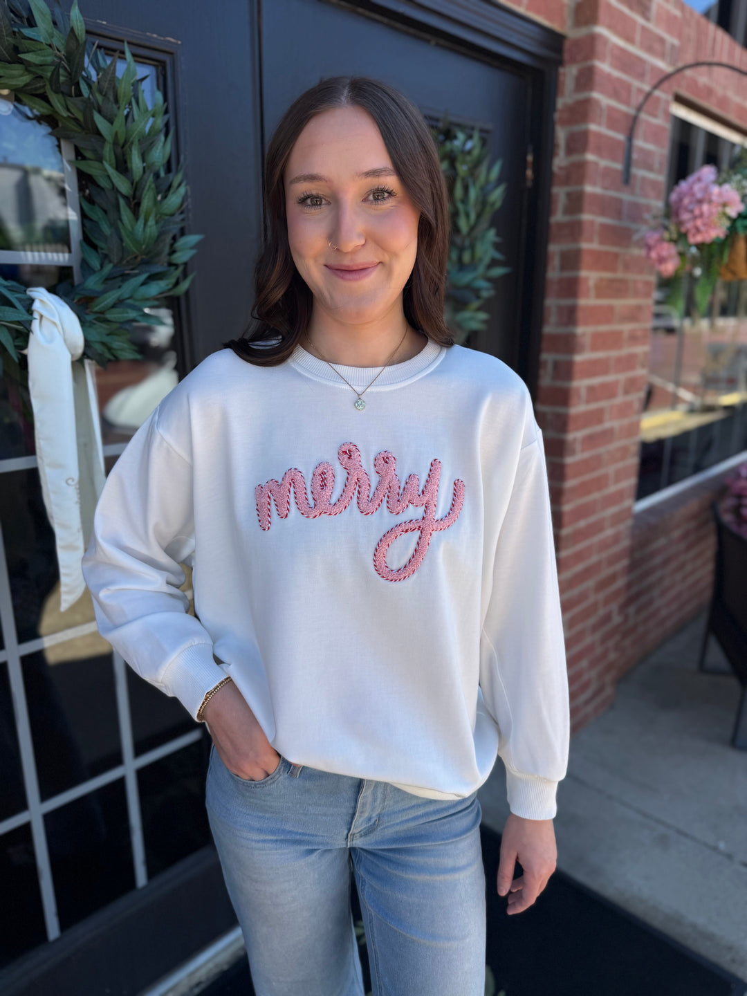 White long-sleeve Sarah Merry Boucle Sweatshirt with pink textured “merry” embroidery. Available in all sizes.