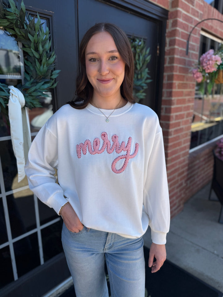 White long-sleeve Sarah Merry Boucle Sweatshirt with pink textured “merry” embroidery. Available in all sizes.